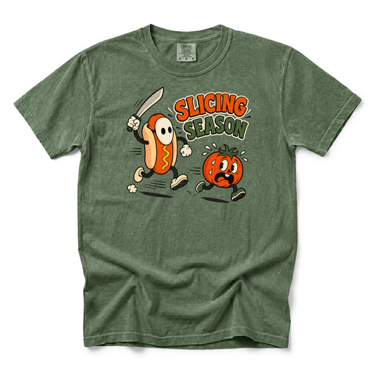 A heathered olive green t-shirt with a cartoon graphic of a hot dog character holding a sword slicing a tomato, with the text 'SLICING SEASON' in orange and green.